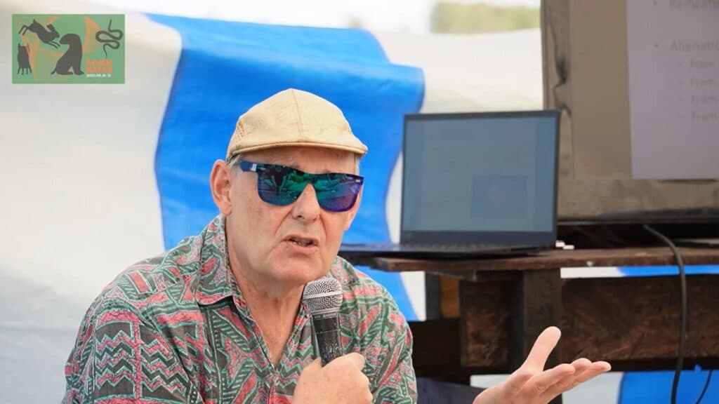Ian Parker, with a cap and dark glasses, in the background of a screen